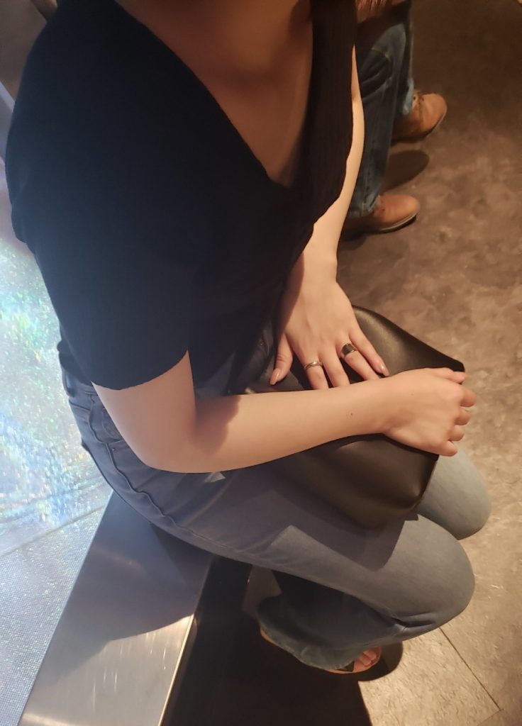 寝取りの伝道師クロエと初対面するセックス好き20代彼女が居酒屋で座る姿。谷間が覗く黒トップス姿で、貸出NTR前の淫靡な緊張感を漂わせる。彼氏不在の中、生ハメ寝取りを許すその直前のシーン。